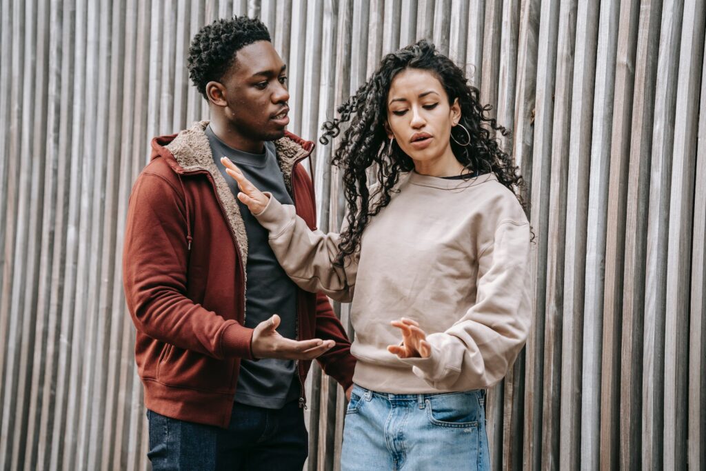 A multiethnic couple engaged in a heated argument on the street, expressing frustration and tension in their relationship.